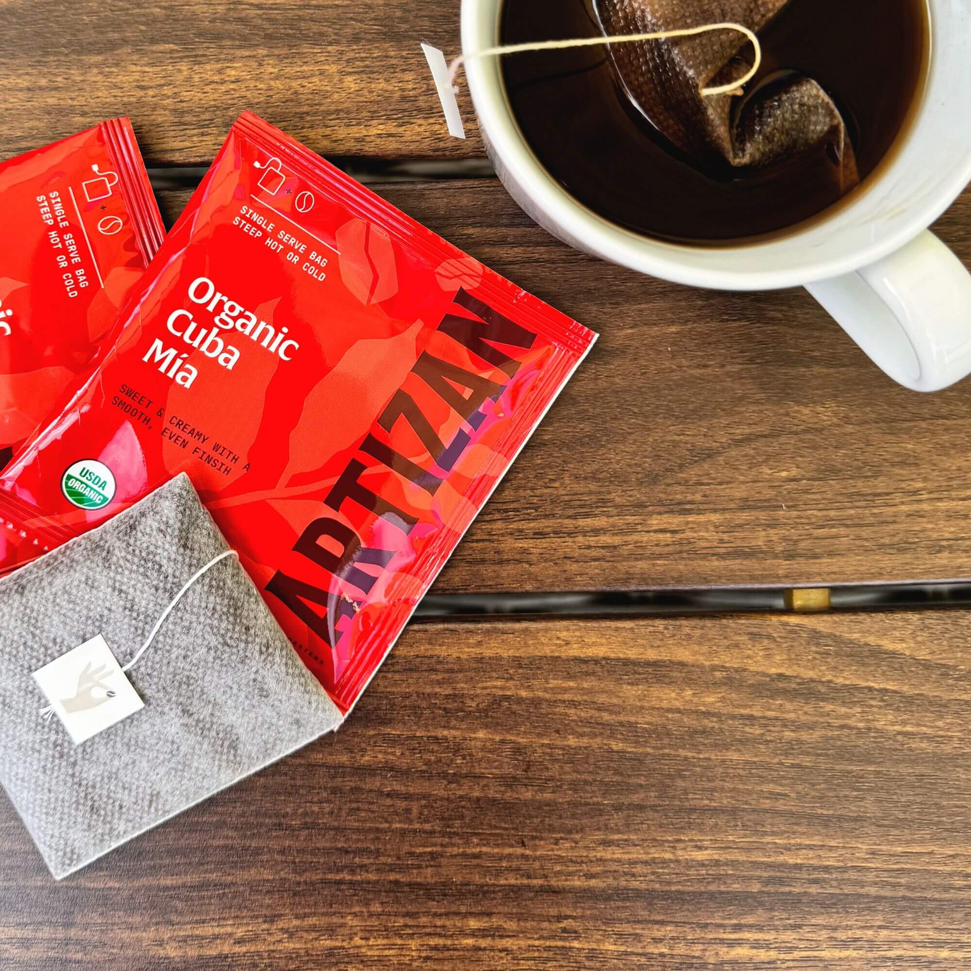 Artizan Coffee Organic Cuba Mia tea bag with red packaging and brewed cup on wooden table