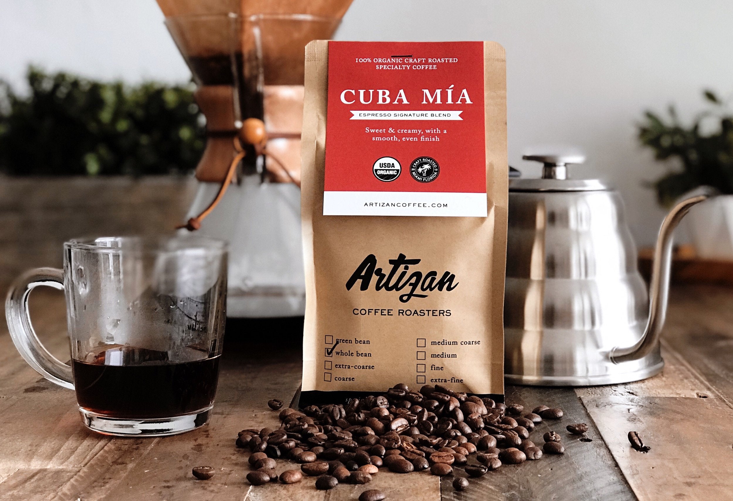 Image of Organic Cuba Mia Whole Bean Bag with Beans on Top of a Wooden Table Beside a Coffee Cup and Coffee Pitcher.