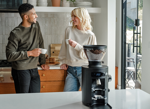 A couple enjoying coffee together in a modern kitchen with a coffee grinder on the counter.