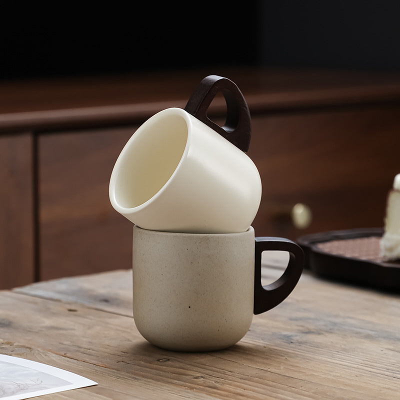 Stacked ceramic mugs in beige and cream colors with unique dark wood handles on a wooden table