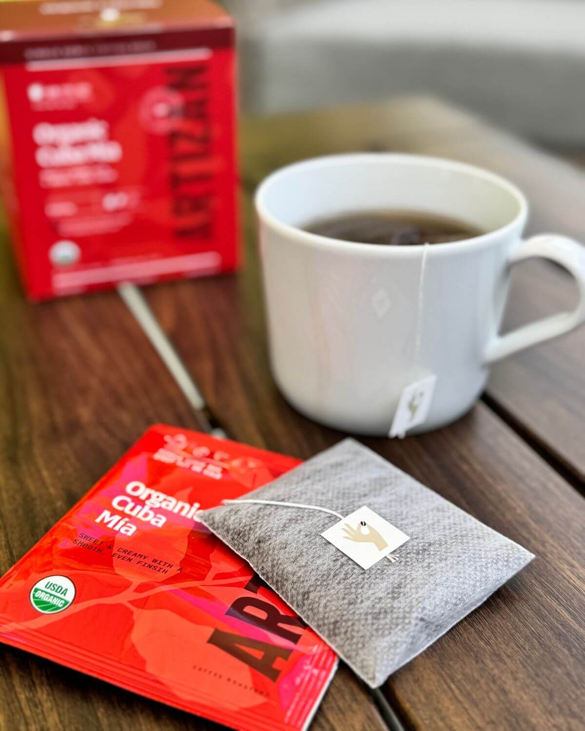Coffee cup with a Cuba Mia Single bag of organic coffee brewing and a package on a wooden surface