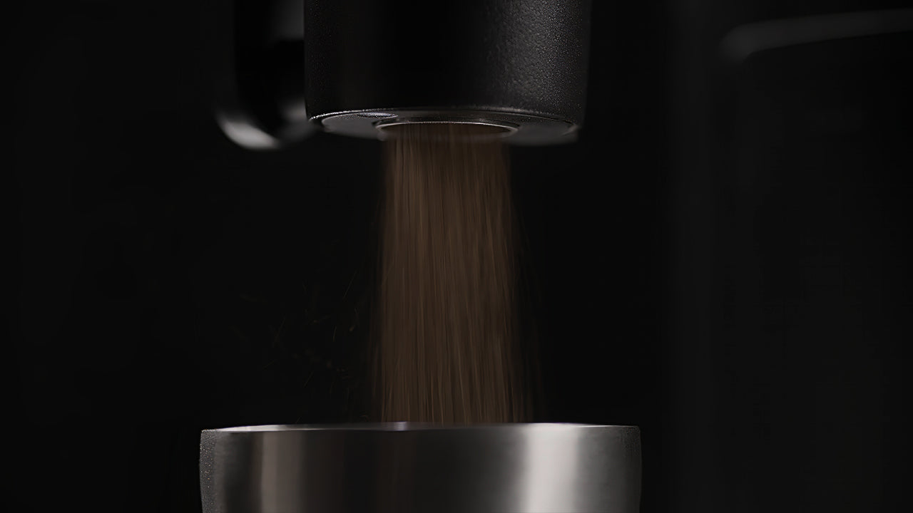 Close-up of coffee grinder dispensing fresh grounds into a portafilter basket with fine, even flow.