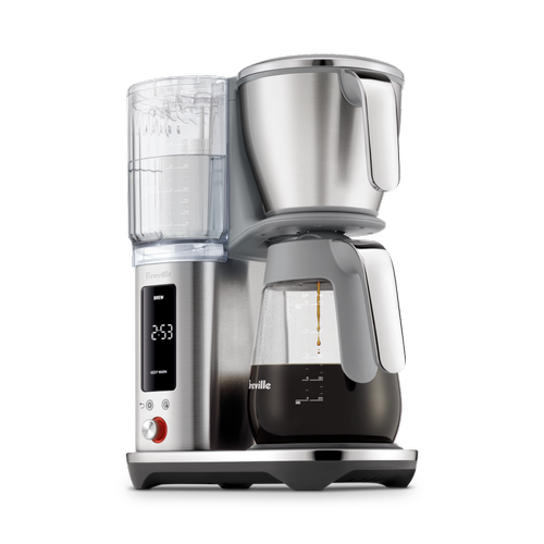 Angled view of The Luxe Brewer Glass drip coffee machine showing clear water tank with measurement markings, stainless steel brew basket, and glass carafe brewing hot coffee.