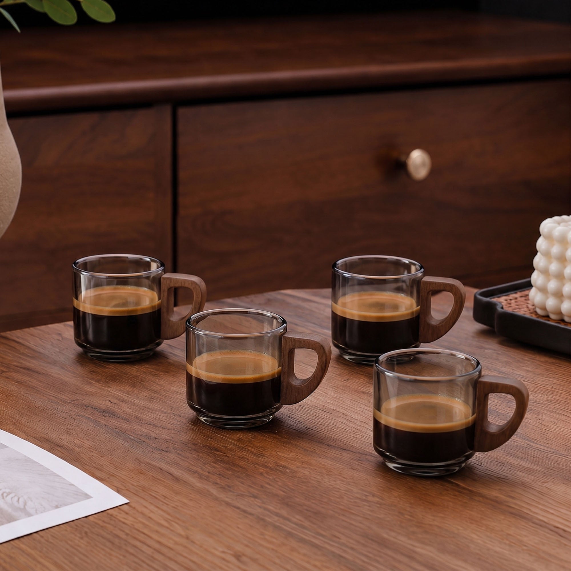 Set of four smoky glass espresso cups with wooden handles filled with espresso on a wooden table.