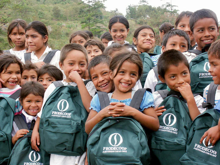 A group of smiling children and community members from the PRODECOOP coffee cooperative in Nicaragua, holding cooperative-branded items and gathered outdoors, reflecting the social impact and community focus of the co-op.