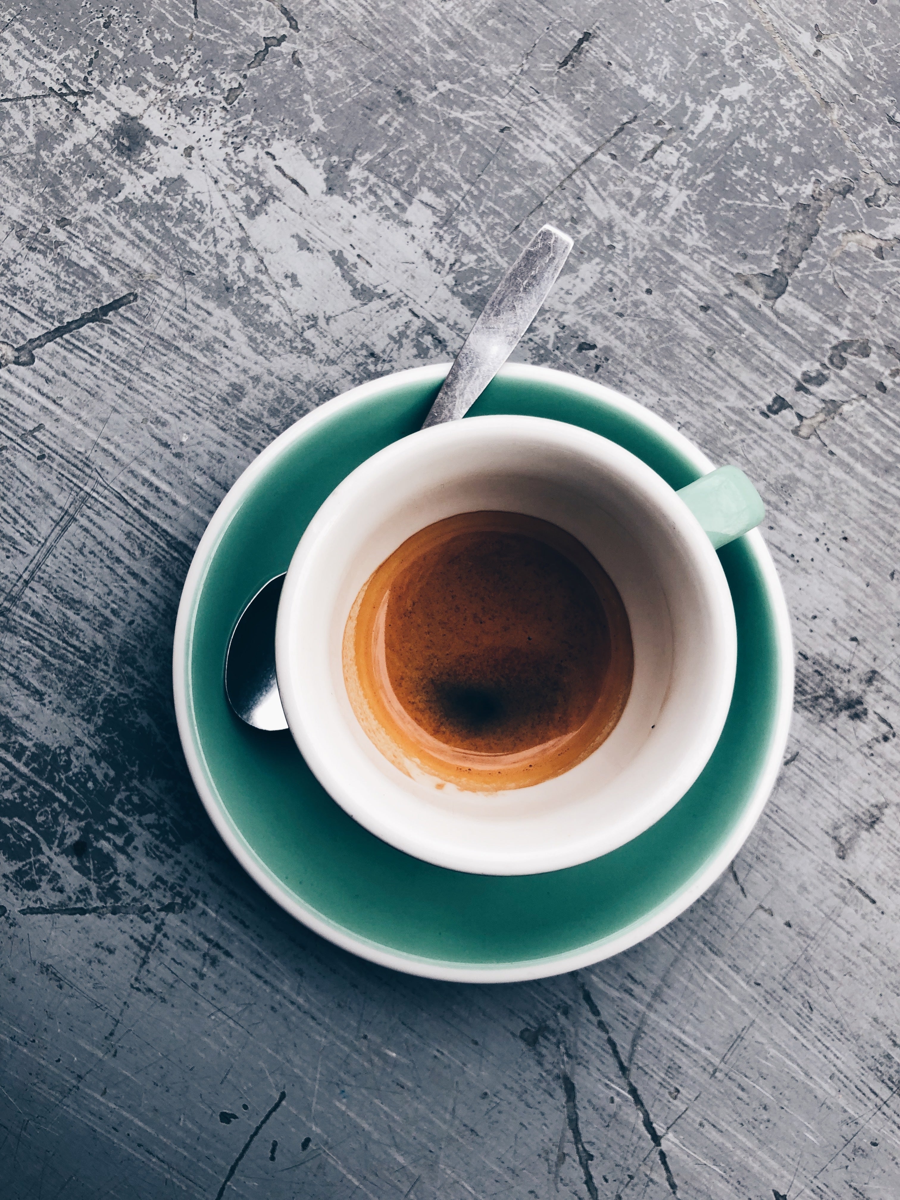 Freshly brewed espresso in white cup with green saucer and spoon on rustic table