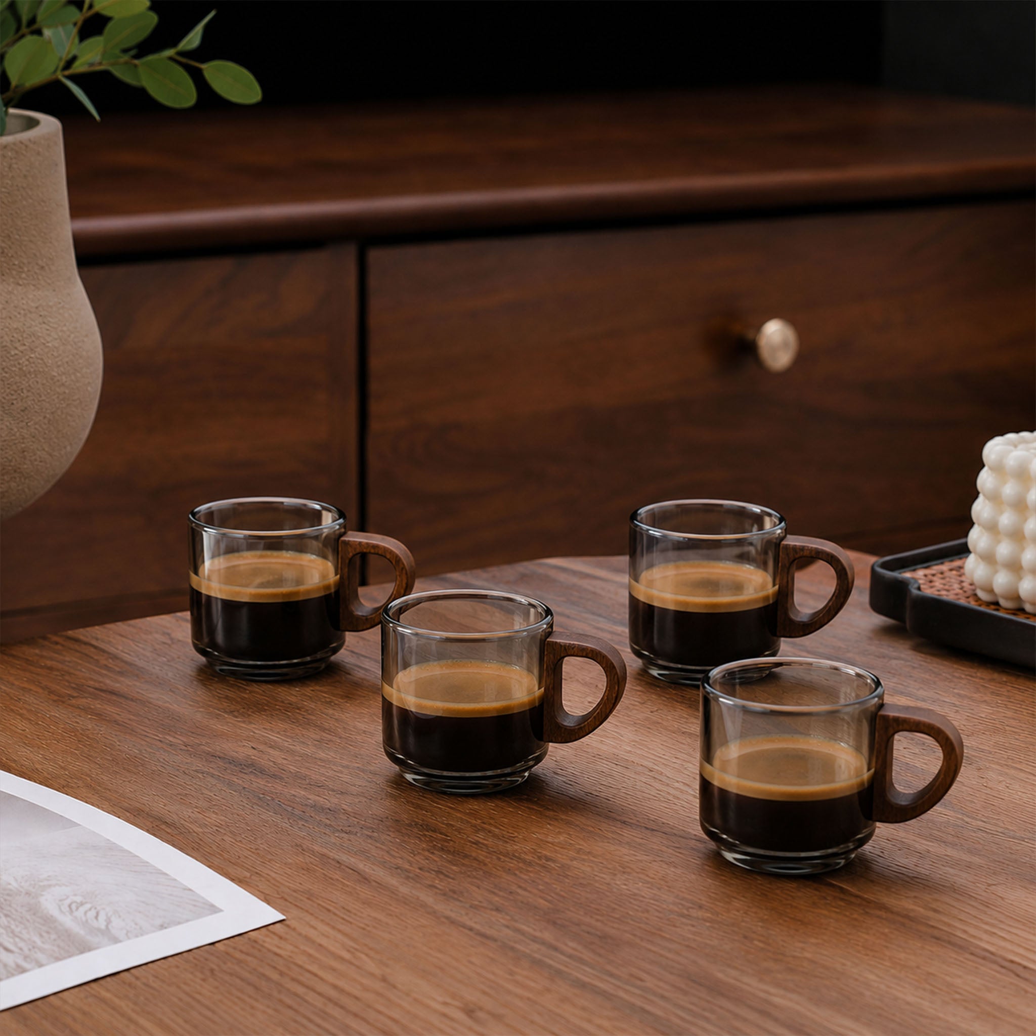 Set of four smoky glass espresso cups with wooden handles filled with espresso on a wooden table.
